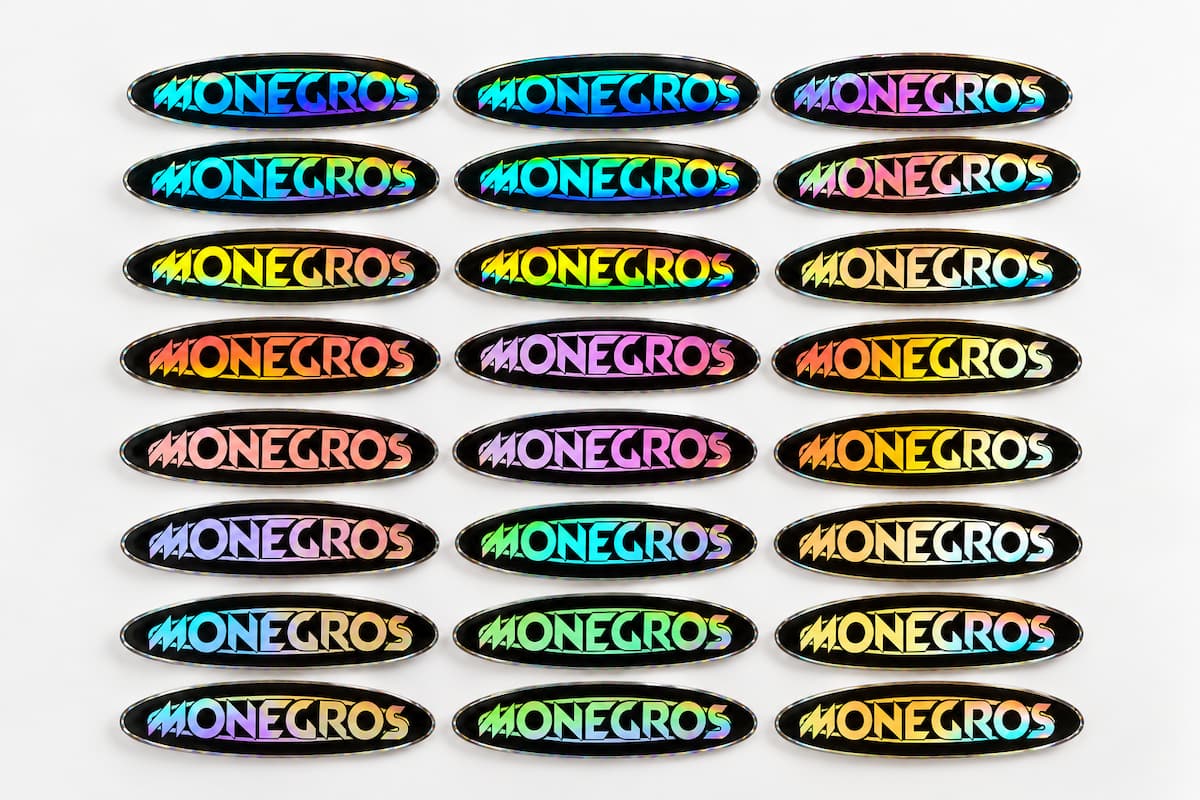 Colección de pegatinas holográficas ovaladas con fondo negro y logotipo multicolor del festival Monegros